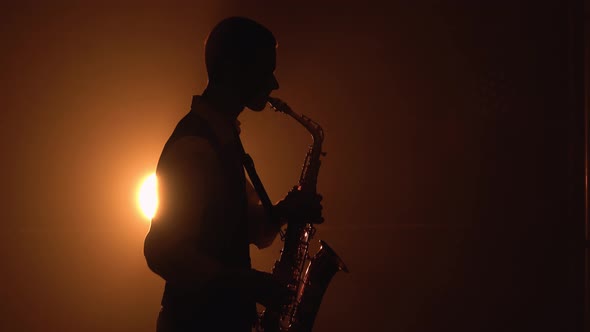 Silhouette a Young Stylish Guy Plays the Golden Shiny Saxophone in the Yellow Spotlights on Stage alt