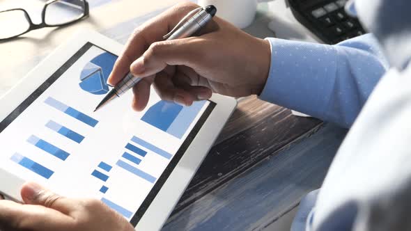 Rear View of Man Hand with Pen Analyzing Charts on Digital Tablet  alt