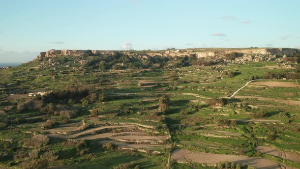 AERIAL: Green Hill Patterned with Farm Lands on a Rocky Mountain Slope in Malta alt