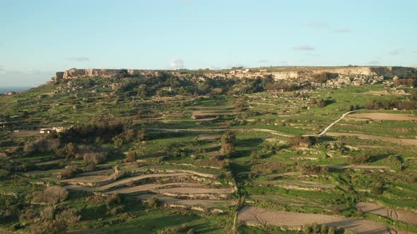 AERIAL: Green Hill Patterned with Farm Lands on a Rocky Mountain Slope in Malta