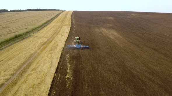 Aerial footage of a tractor plowing black agriculture farm field after harvesting in autumn alt
