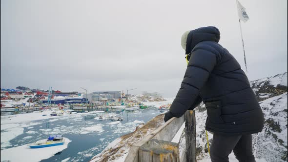 Man In Winter Coat Looking Over Town Of Ilulissat alt