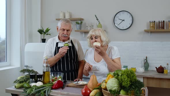 Senior Couple in Kitchen. Elderly Grandmother and Grandfather Eating Raw Broccoli and Cauliflower alt