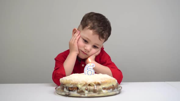 Upset White Child on His Birthday. Alone Child Sits in Front of Cake with Candles.