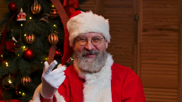 Portrait of Santa Claus Looking at the Camera Waves Hello and Makes Gesture Come Here alt