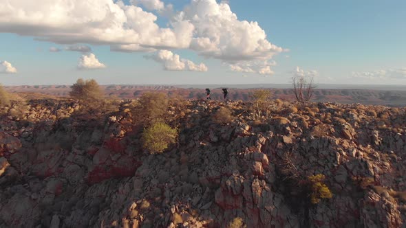Aerial pan, hikers on rocky mountain ridge, blue sky and white clouds alt