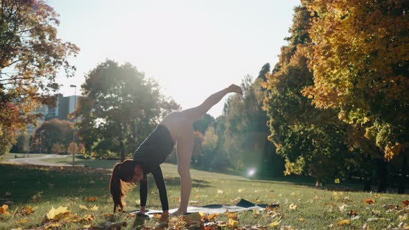 Young Woman Practices Yoga Poses in Autumn City Park on a Yoga Mat