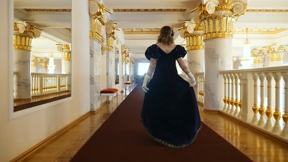 Woman in an Elegant Dress Walks Along the Golden Corridor of the Theater