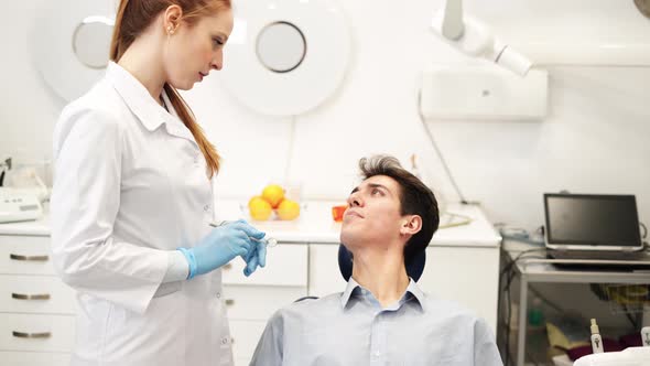 Young Attractive Female Dentist Talking with Man Sitting in Dental Chair About Teeth Problems alt