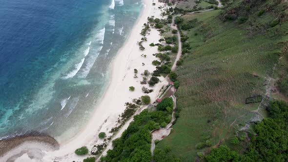 Green hills, while sand, blue ocean and rolling waves of remote destination- aerial drone shot of ba alt
