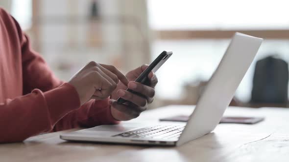 Hands Close up of African Man with Laptop using Smartphone alt
