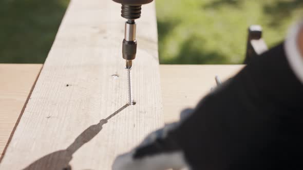 Slow motion of a man using an electric screwdriver to drive a screw into wood