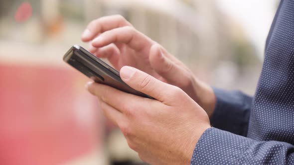 A Man Works on a Smartphone in an Urban Area  Closeup  a Street in the Blurry Background