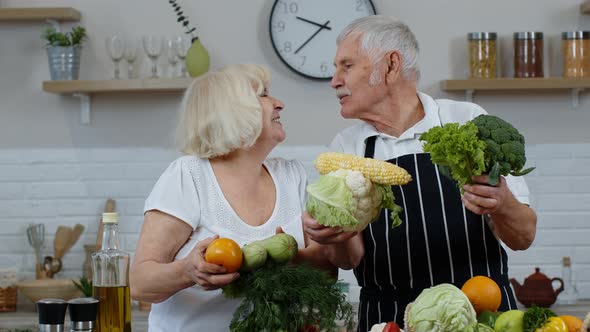 Senior Grandparents Couple in Kitchen. Mature Man and Woman Recommending Eating Raw Vegetable Food alt