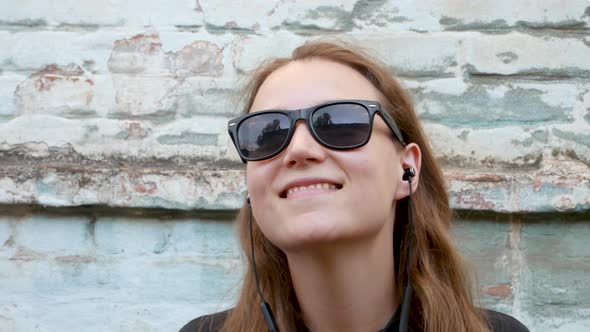 Young attractive girl in black t-shirt sunglasses rock style on urban background listening to music