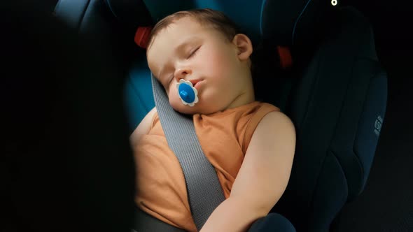 A Little Boy Sleeps in a Chair. Children's Safety Systems in Cars.