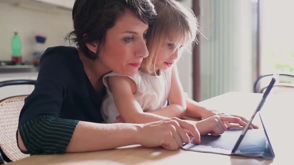 Adult woman mother teaching female child using tablet computer alt