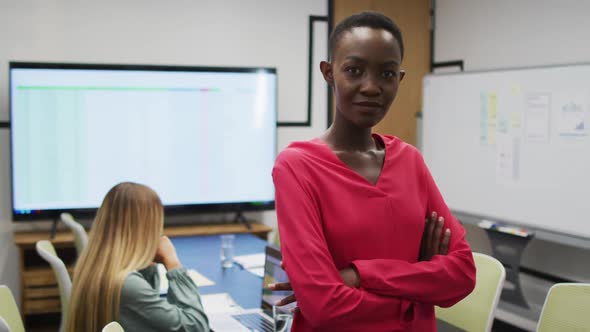 Portrait of african american businesswoman smiling in office, with colleague working in background alt