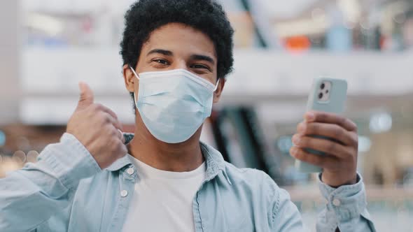 Portrait Satisfied African Guy in Protective Medical Mask Man Looking at Phone Smartphone Showing alt