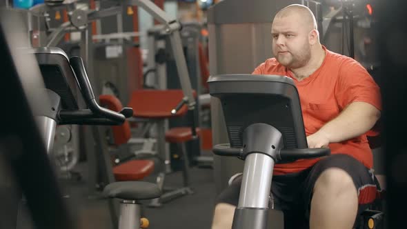 Overweight Man Is Training on Bicycle at Fitness Club