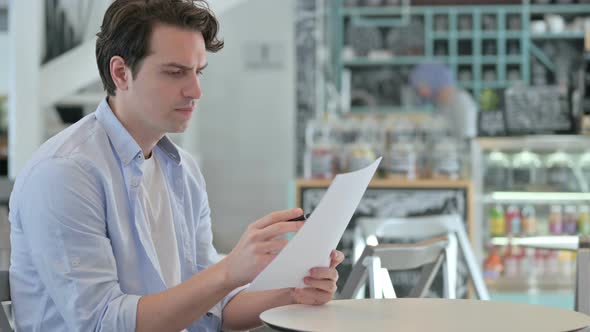 Young Man Reading Documents in Cafe alt