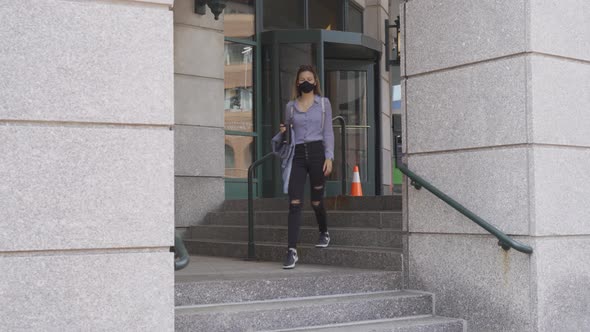 Slim woman walks down steps wearing black face mask to stop covid-19 spread alt