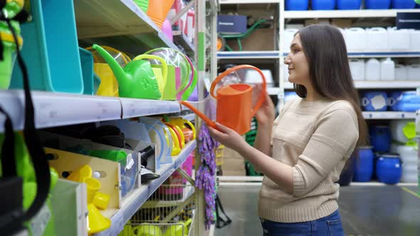 Young Woman Examines Watering Cans in the Store alt