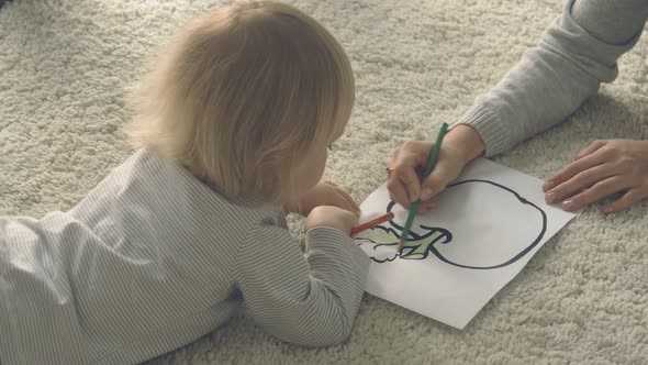 Baby girl with mother paints picture with pencils alt