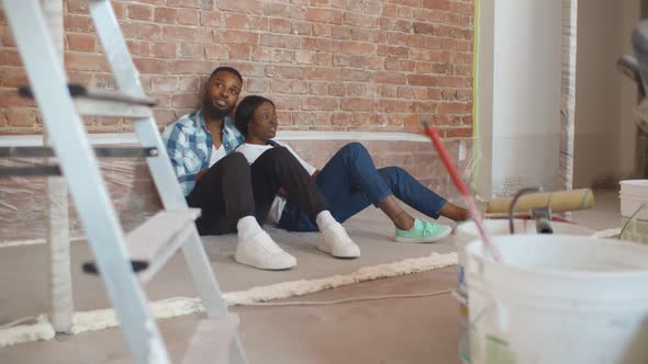 African Couple Sitting on Floor in Empty Room of New Home Planning Design alt