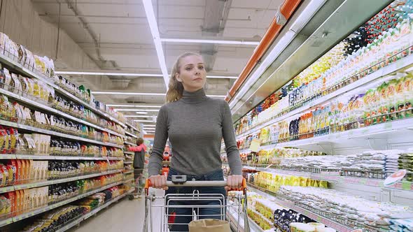 Young Female Walks Between the Shelves in a Grocery Store Visiting a Supermarket a Woman Walks with alt
