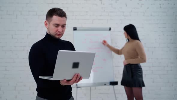 Young man and woman in the studio. Handsome man working on a laptop while woman is writing on a whit alt