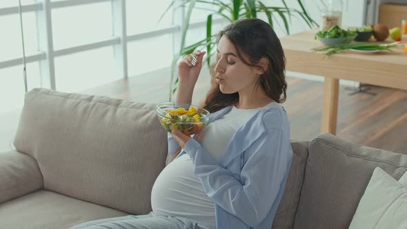 Pregnant Woman With Great Pleasure Eating Vegetable Salad on the Couch alt