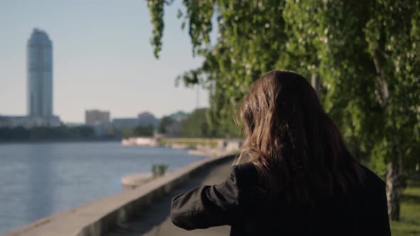 A Woman Rushing To Work Walks Along the Park Along the City Embankment alt
