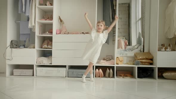 Dancing Little Girl Enjoy New Dress in Clothing Room on Backdrop of Wardrobe with Clothes