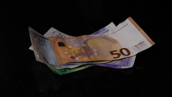 Different banknotes with a 50 euro on top falls in slow motion on a black surface. alt
