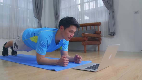 Man Doing A Plank While Watching Online Tutorial On Laptop, Exercising In Living Room alt