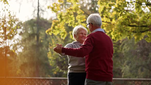 Senior Caucasian Couple Slowly Dancing in the Park Smiling at Each Other and Enjoying Beautiful