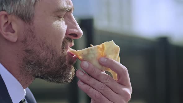 Grey haired man biting pizza and drinking coffee