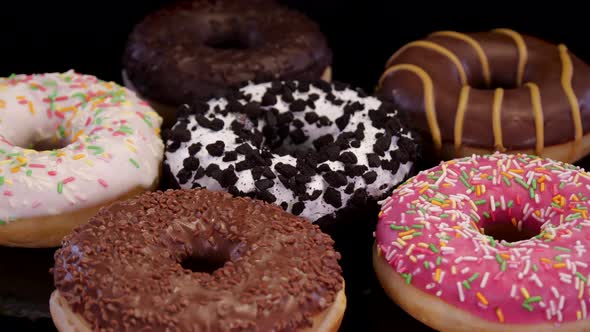 Various donuts with icing and colorful sprinkle rotating on a black background.