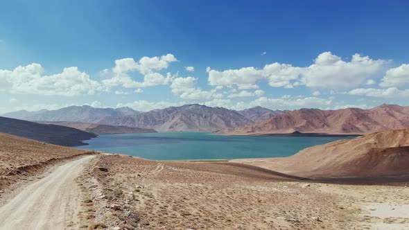 Aerial Over Gravel Road Path Toward Bulunkul Lake in Sunny Day alt