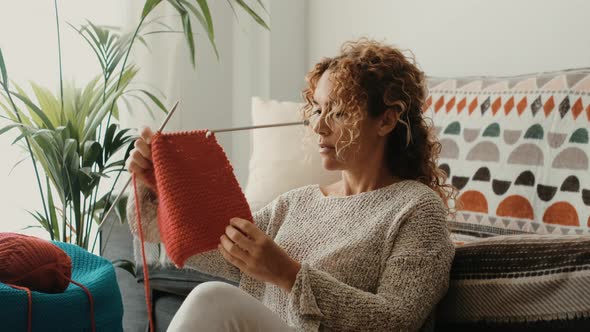Young woman picking wool from basket while sitting on floor at home. Beautiful woman knit work alt