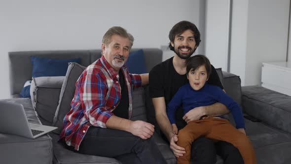 Portrait of Happy Caucasian Three Generation Men Smiling to the Camera at Home Sitting on Sofa alt
