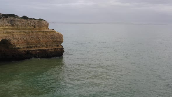 Rocky cliffs in Fontainhas beach of South Portugal appearing from the side, Aerial dolly in reveal s alt