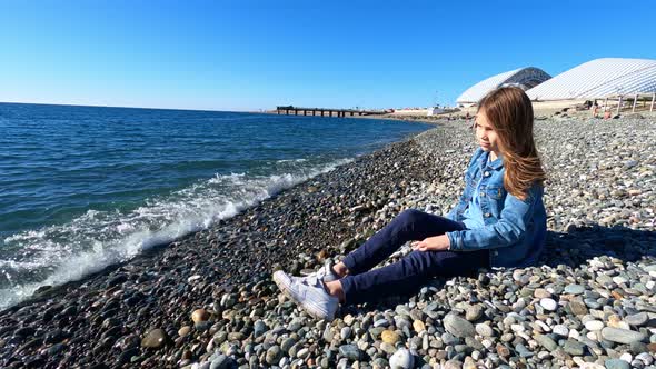 Girl Throws Stones Into Water and Jokes While Sitting on Sea Shore alt