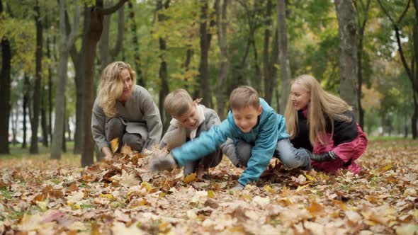 Wide Shot of Joyful Carefree Mothers and Sons Tossing Yellow Leaves in Autumn Park alt