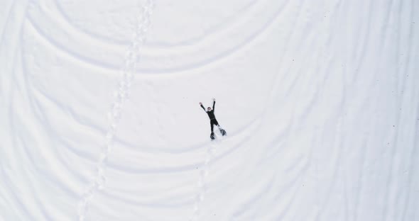 Overhead Aerial Top View Over Man Lying Doing Snow Angel with Snowshoes on White Covered Snowy Field