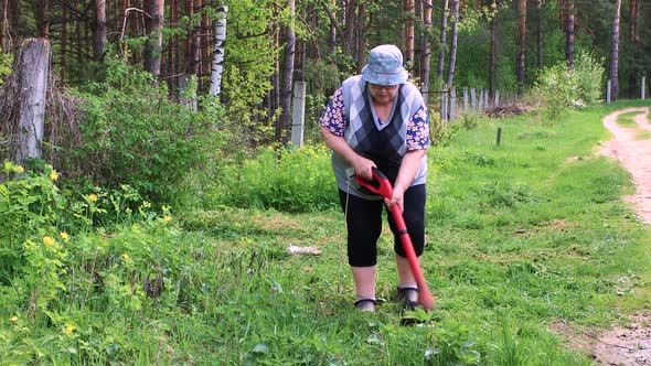 A Woman Mows Low Green Grass with an Electric Trimmer alt