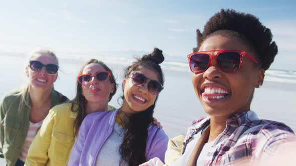 Happy group of diverse female friends having fun, taking selfie with smartphone at the beach alt