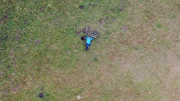 woman laying on green grass in park with bicyle near, resting, aerial shot