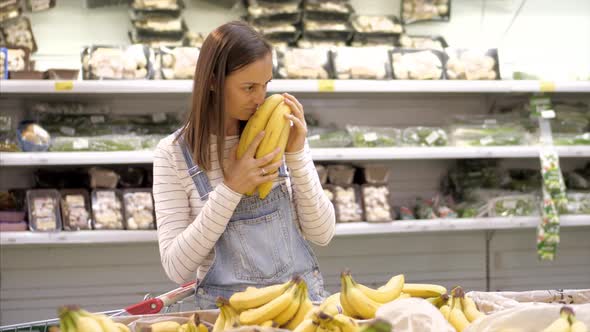 Young Woman in Denim Overall is Selecting Fresh Bananas at Grocery Store